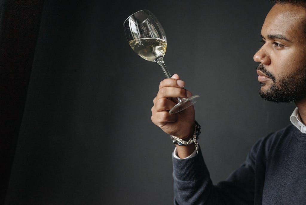 A man carefully examines a glass of white wine in a sophisticated atmosphere.