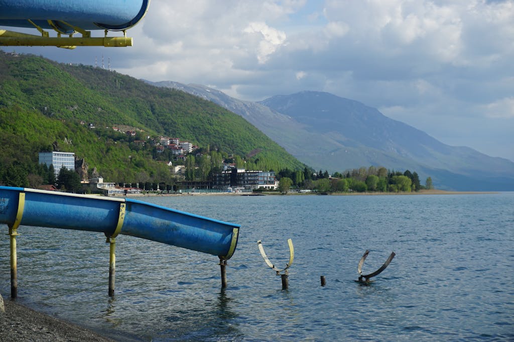 Serene Lake Ohrid with lush green hills and a water slide under a cloudy sky.