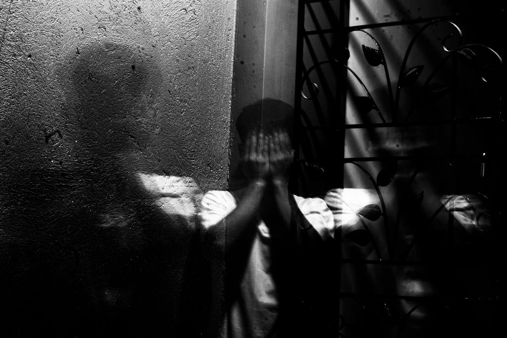 Grayscale image of a man covering his face, evoking themes of fear and introspection.